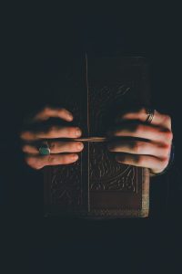 Book of Shadows held by two hands against a black background
